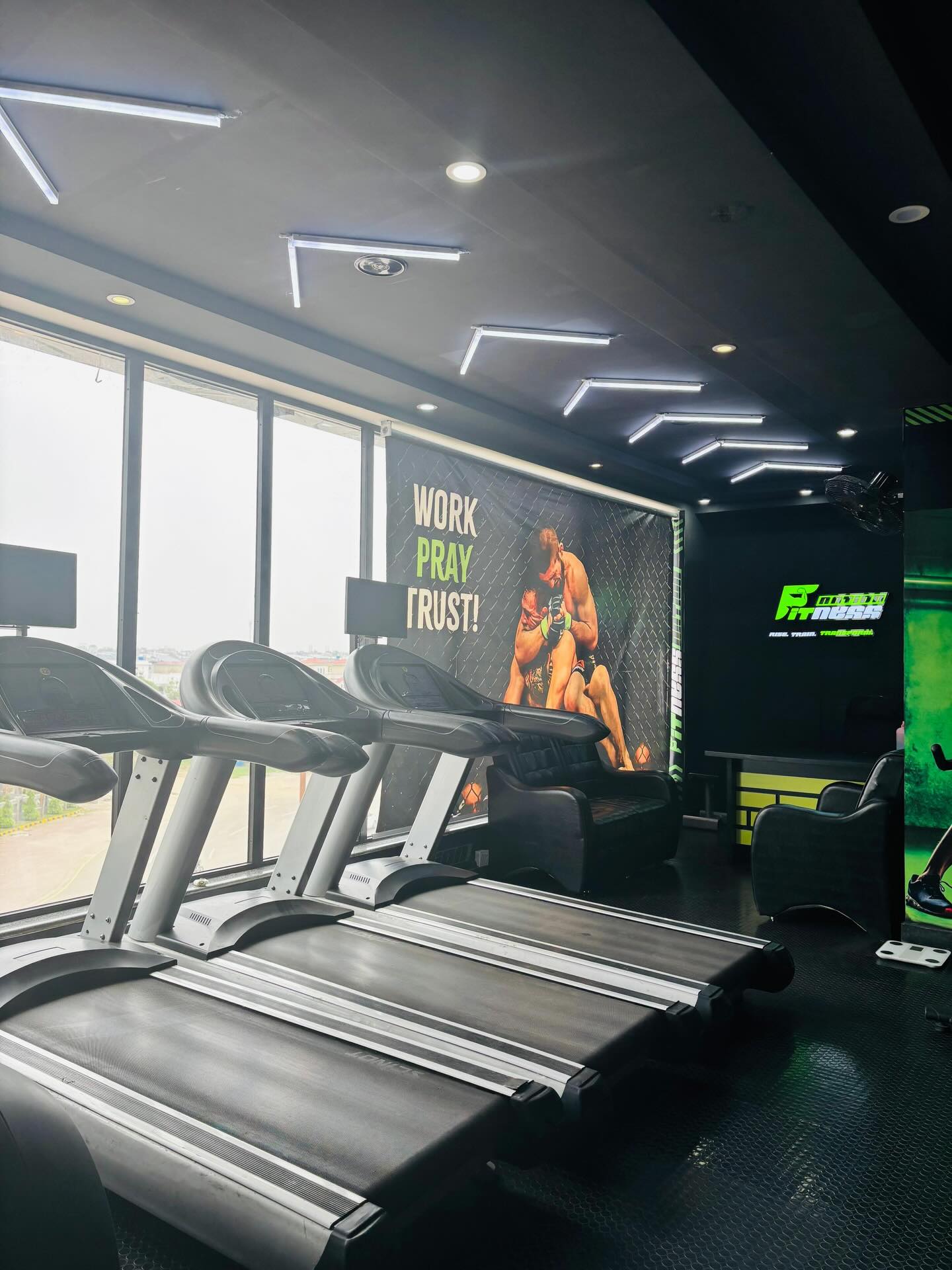 Treadmills facing the windows with the Work · Pray · Trust mural